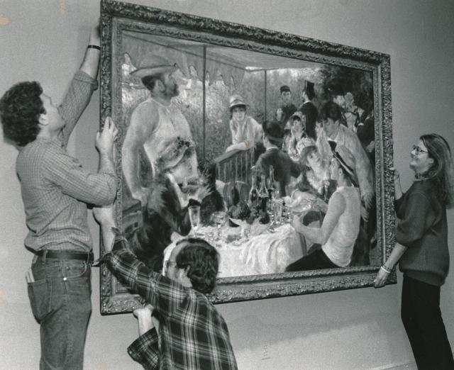 Black and white photograph of three people hanging up Renoir's Luncheon of the Boating Party