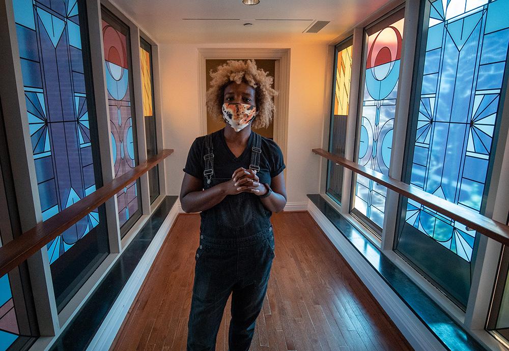 Photo of Nekisha Durrett standing in the Phillips bridge with her stained-glass inspired artwork on the windows