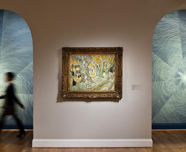 Photo of a figure walking in front of walls with drawings by linn meyers, with a painting by Van Gogh on display 