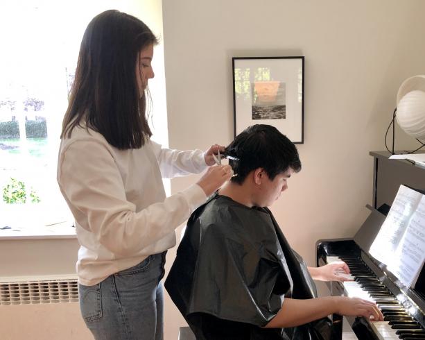 Photo of someone cutting the hair of someone that is playing the piano