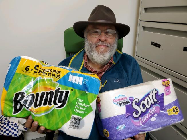 Photograph of man holding packages of toilet paper and paper towels