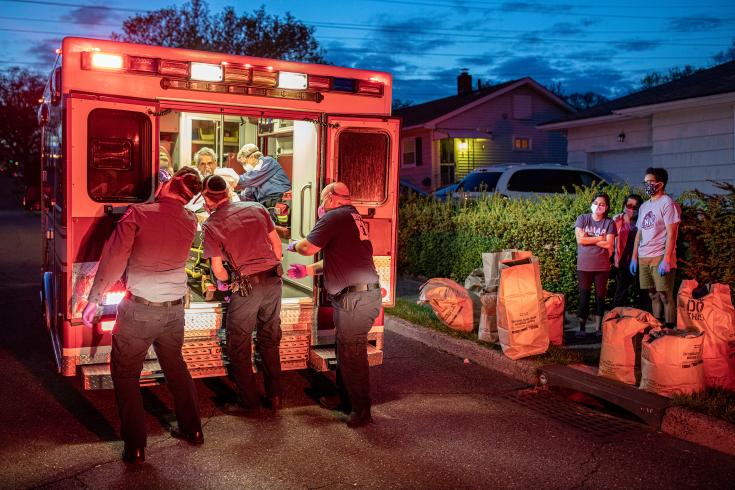 Photograph of EMS volunteers helping someone into an ambulance in front of a house