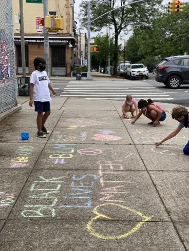 Photograph of four people writing in chalk on the sidewalk