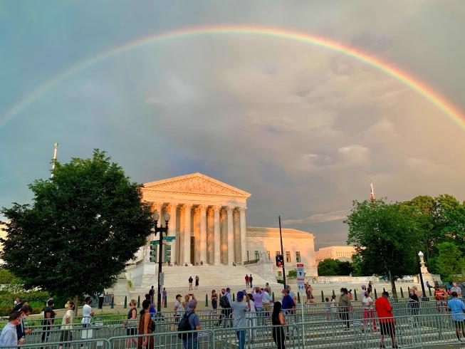 Photograph of people in socially distanced lines, waiting to pay respects to Representative John Lewis are treated to a rainbow over the Supreme Court.