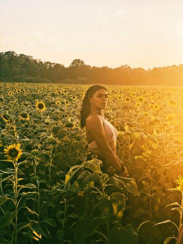 A person standing in a field of flowers, with the sun shining
