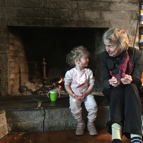 Photograph of a small child sitting with their grandmother next to a fireplace