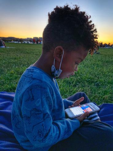 Photograph of a child looking at an iPhone, on a grassy field