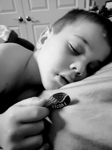 Photograph of a young boy asleep, with an "I Voted" sticker in his hand