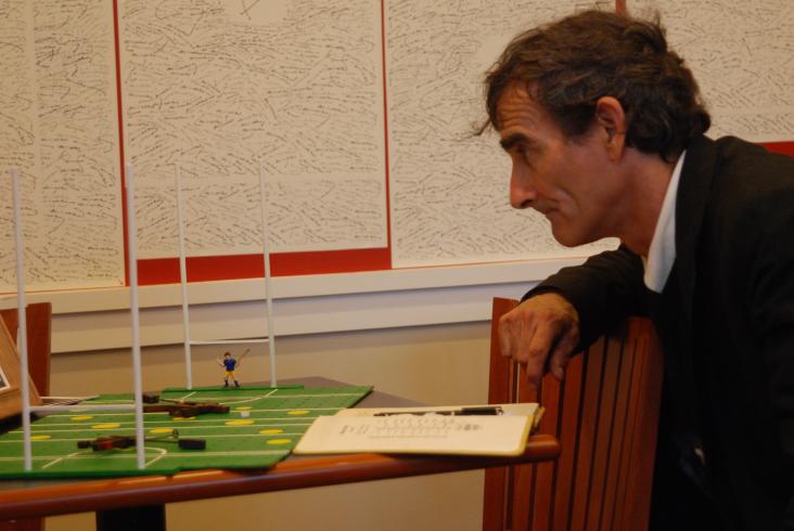 A man stares at a miniature football pitch which sits on a table.