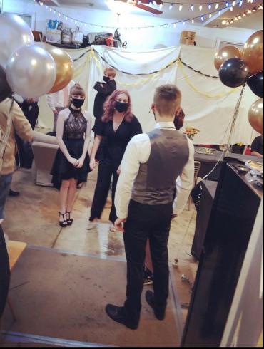 Photograph of a small group of high school students dressed up for a dance in a garage, with masks on, due to covid