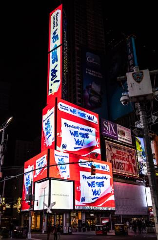 Photograph of a building covered in digital signs with the sign in red and white that says "We See You"
