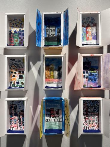 9 cardboard windows with colorful drawings of city scenes.