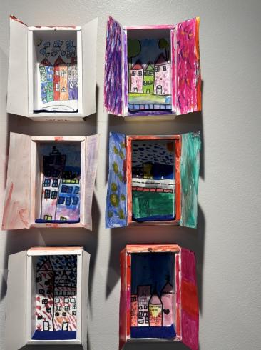 6 cardboard windows with colorful drawings of city scenes.