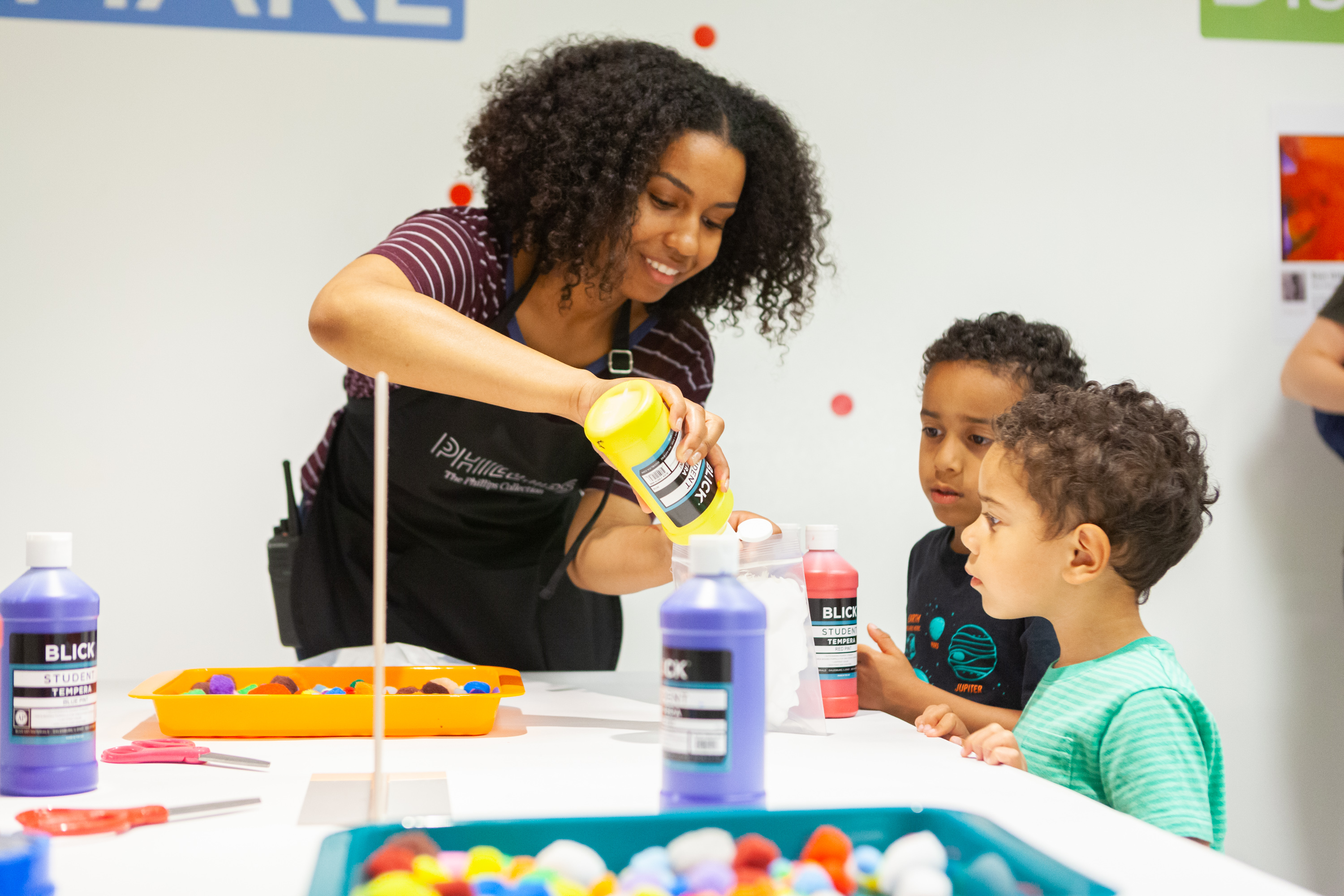 Photograph of a woman helping two small children prepare paints