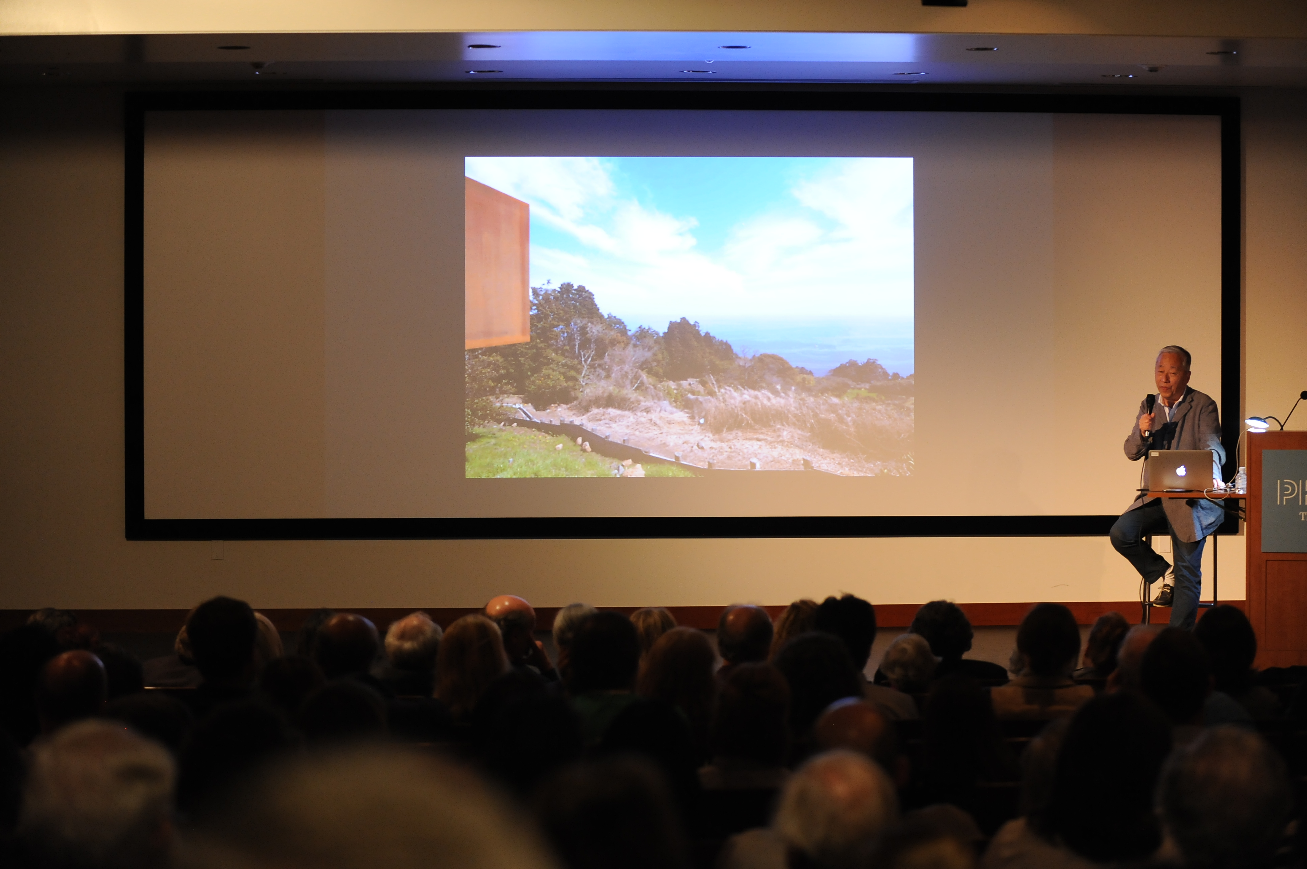 Photograph of Hiroshi Sugimoto on stage next to a podium giving a talk in an auditorium