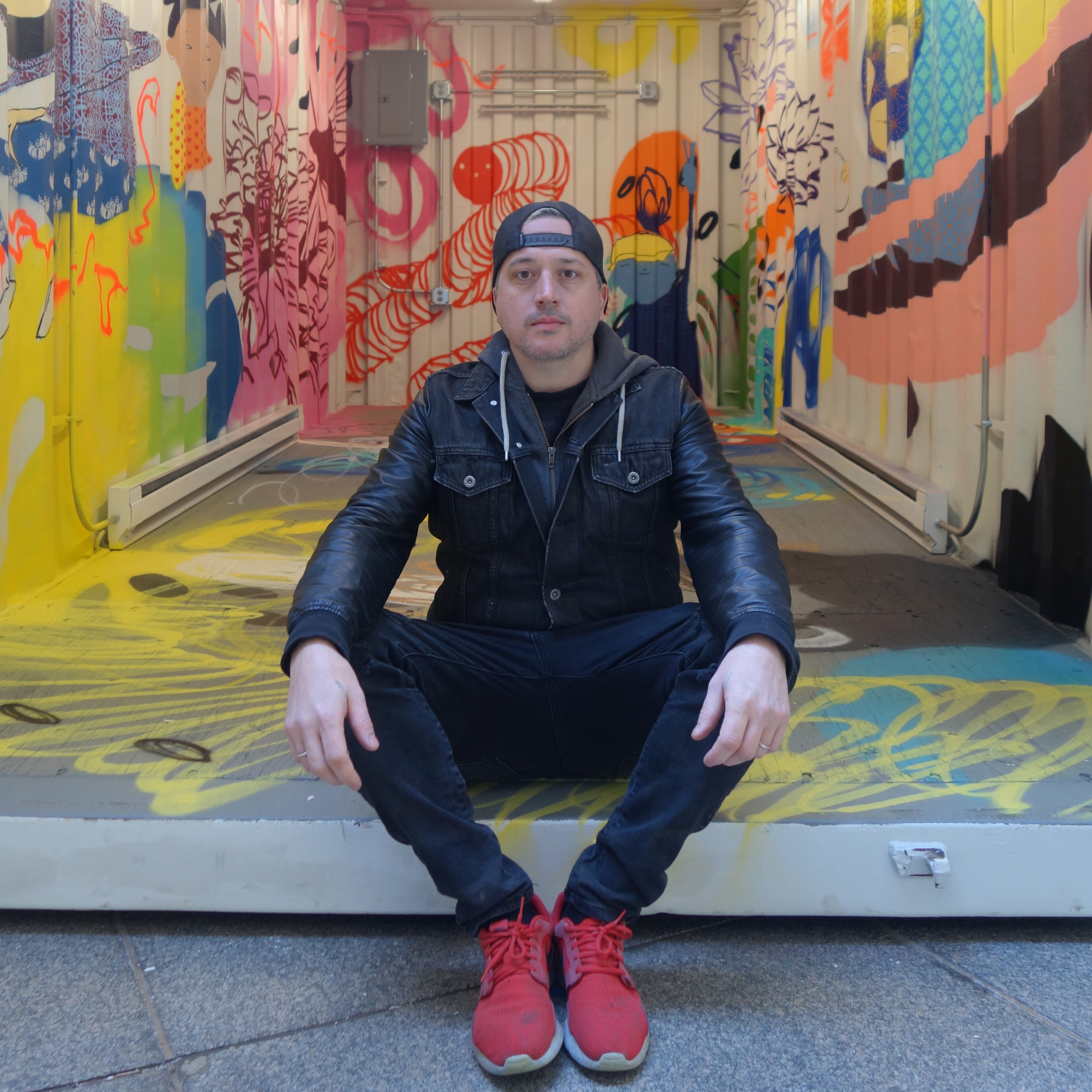 Photo of Kelly Towles sitting on the ground with colorful murals behind him