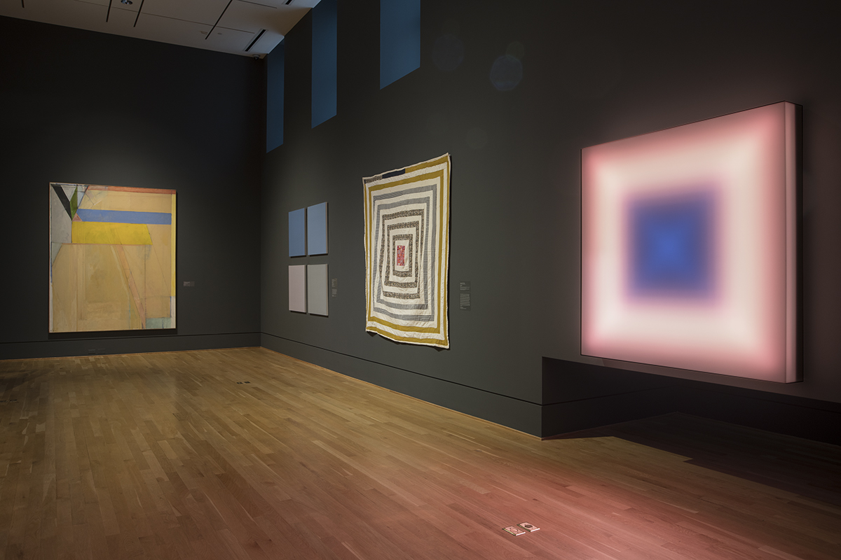 Photograph of four colorful artworks in a museum gallery with dark blue walls
