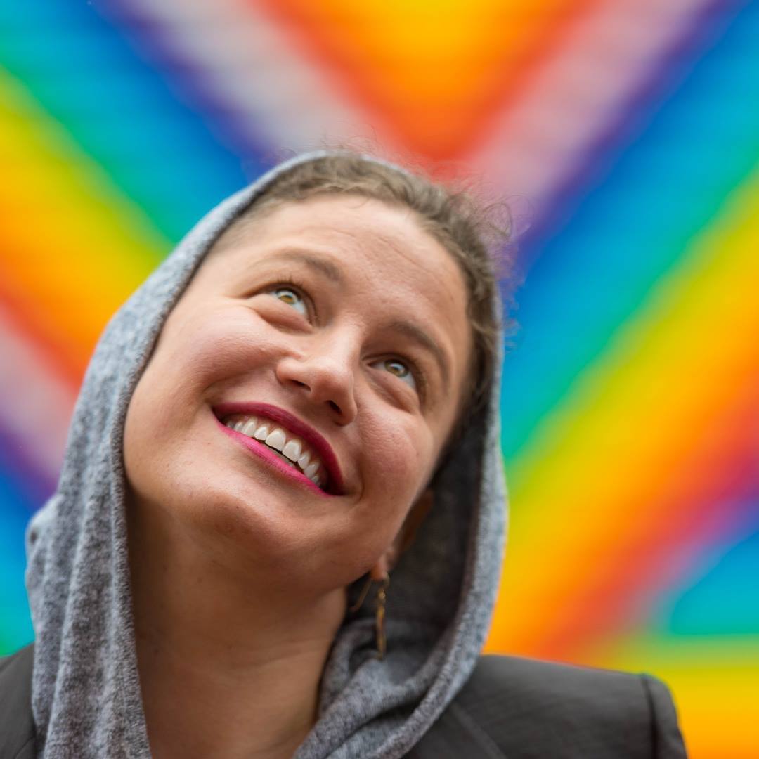 Photo of Lisa Marie Thalhammer smiling with a rainbow background