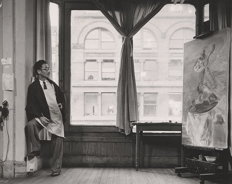 Photograph of Yasuo Kuniyoshi standing in his studio looking at a painting