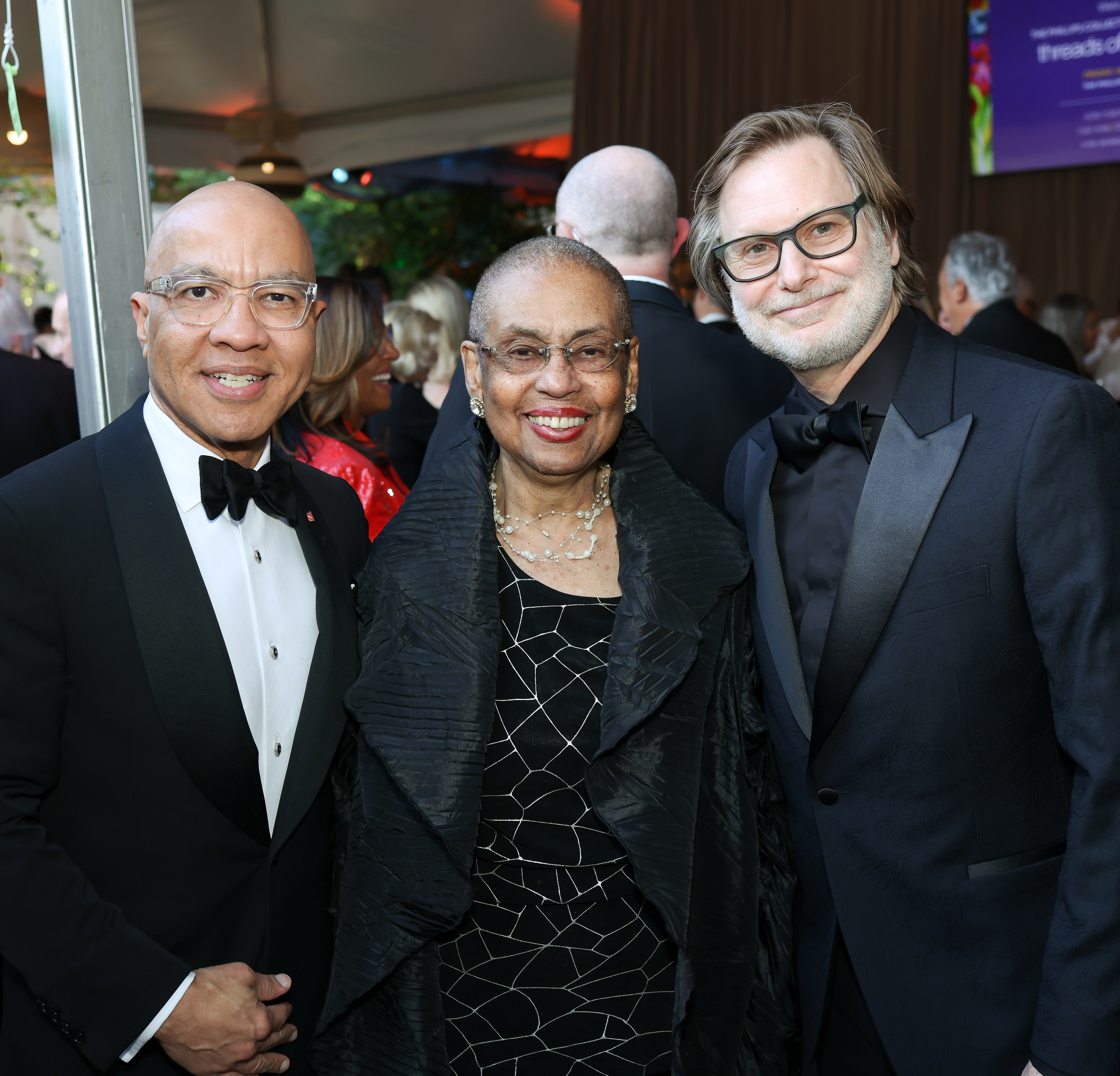 Photograph of three people in black-tie standing together smiling at camera