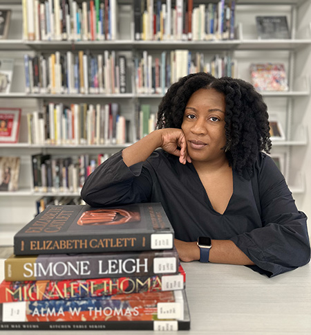 Photograph of Elizabeth Ajunwa sitting at a table with her elbow on a stack of books
