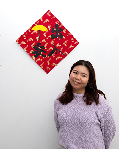 photograph of Amity Chan standing next to one of her artworks on a wall