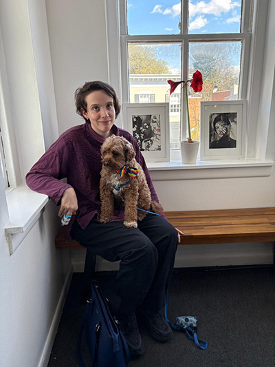 Photograph of Celine Krempp sitting in a room with large windows with a dog in her lap