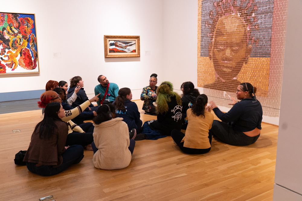 Group of people sitting on the floor in a gallery with art on the walls