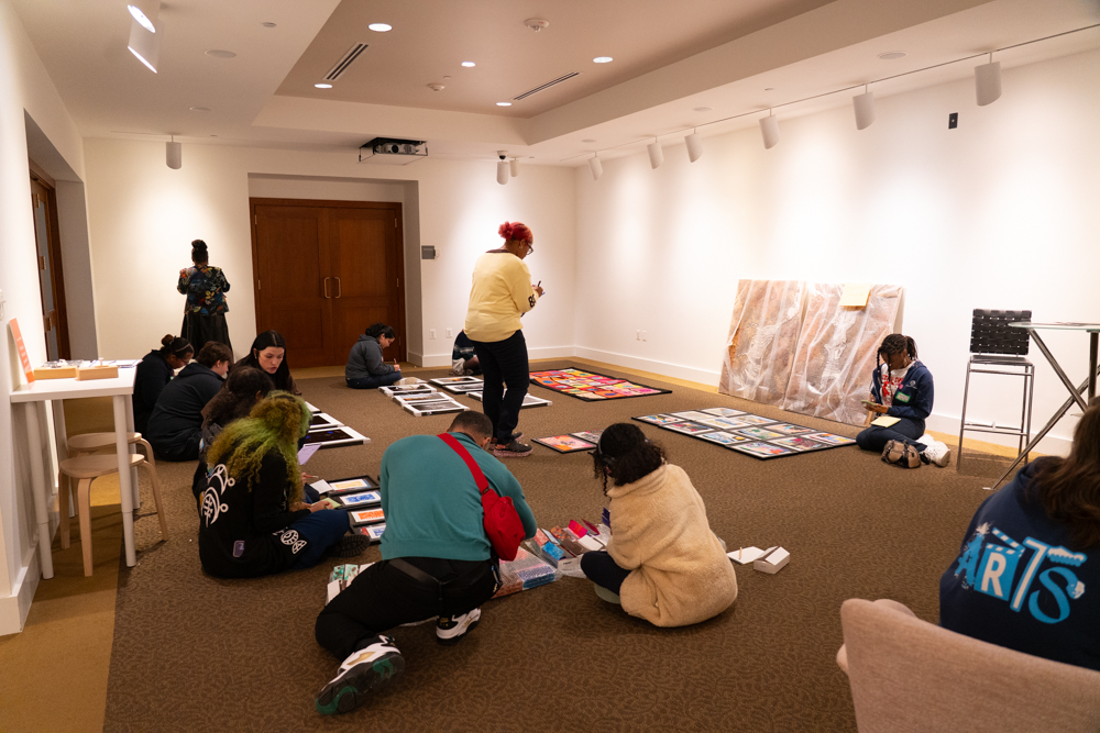 Group of people looking at artworks laid out on the floor