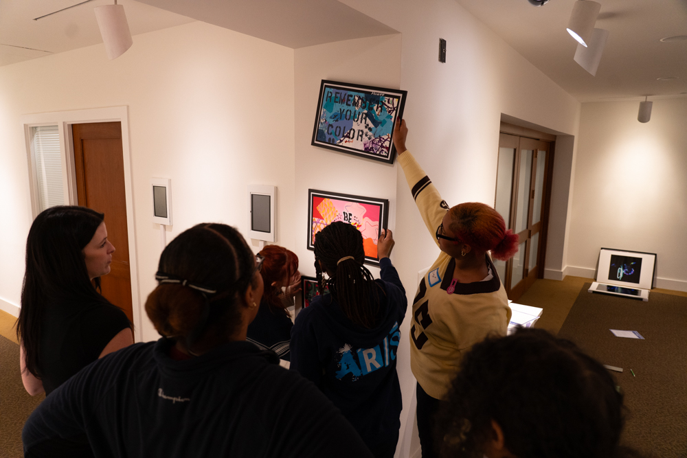 Group of people looking at someone holding an artwork up on a wall