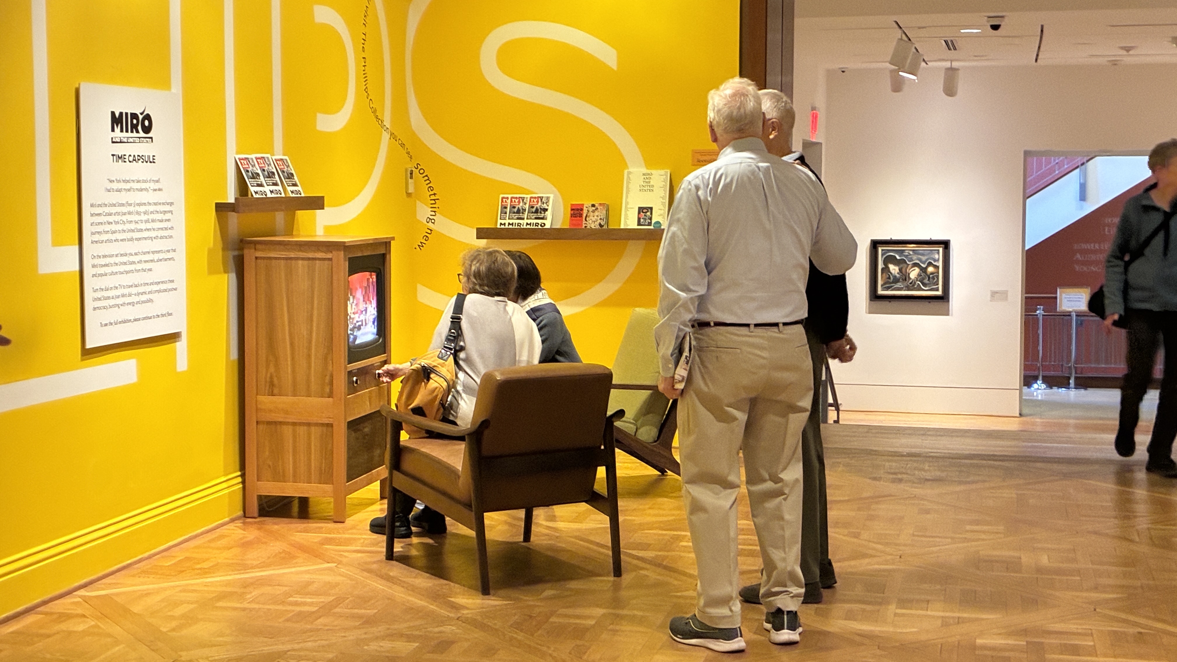 Two people standing and 2 people sitting looking at the Miro tv station