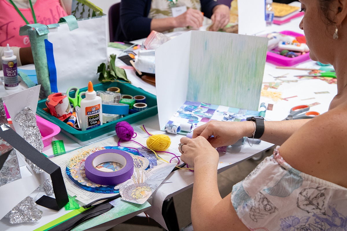Close up of people sitting at a table creating artwork with lots of various materials