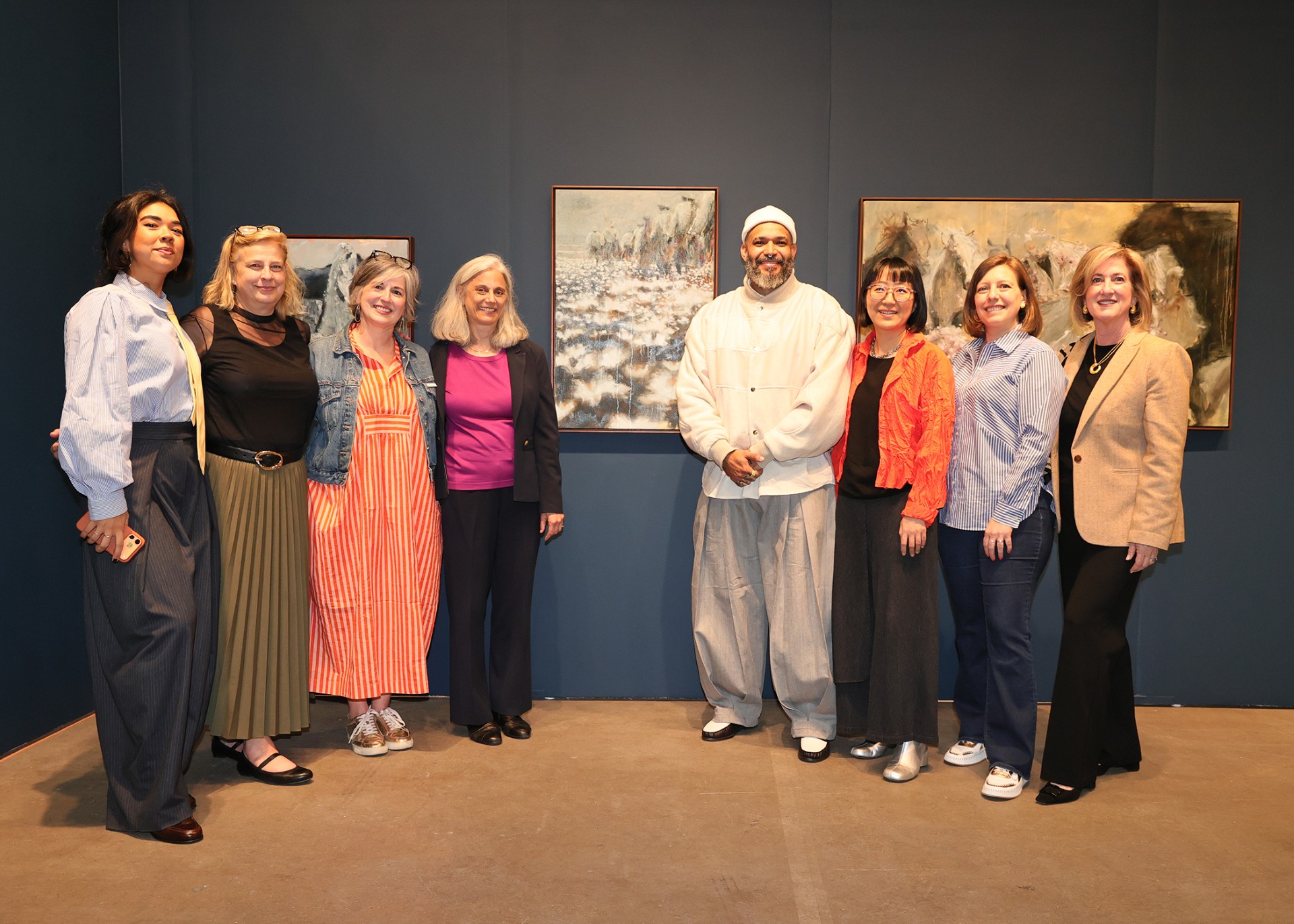Photograph of a group of 8 people standing next to an artwork displayed on the wall