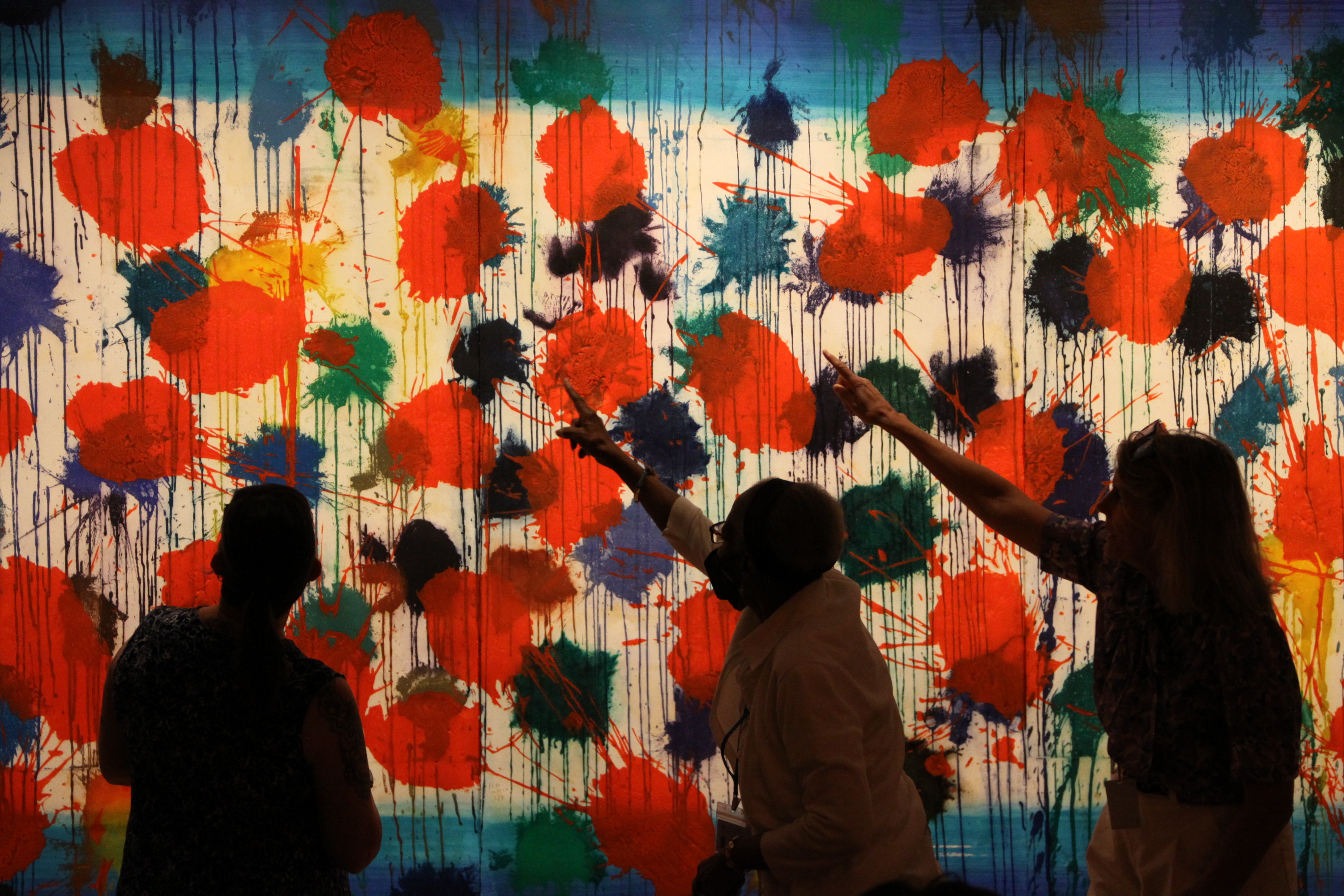Three people standing in front of a large colorful artwork