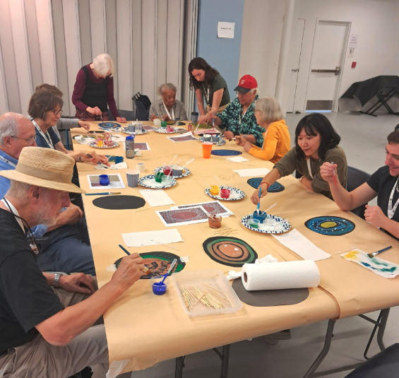People sitting and standing around a table painting