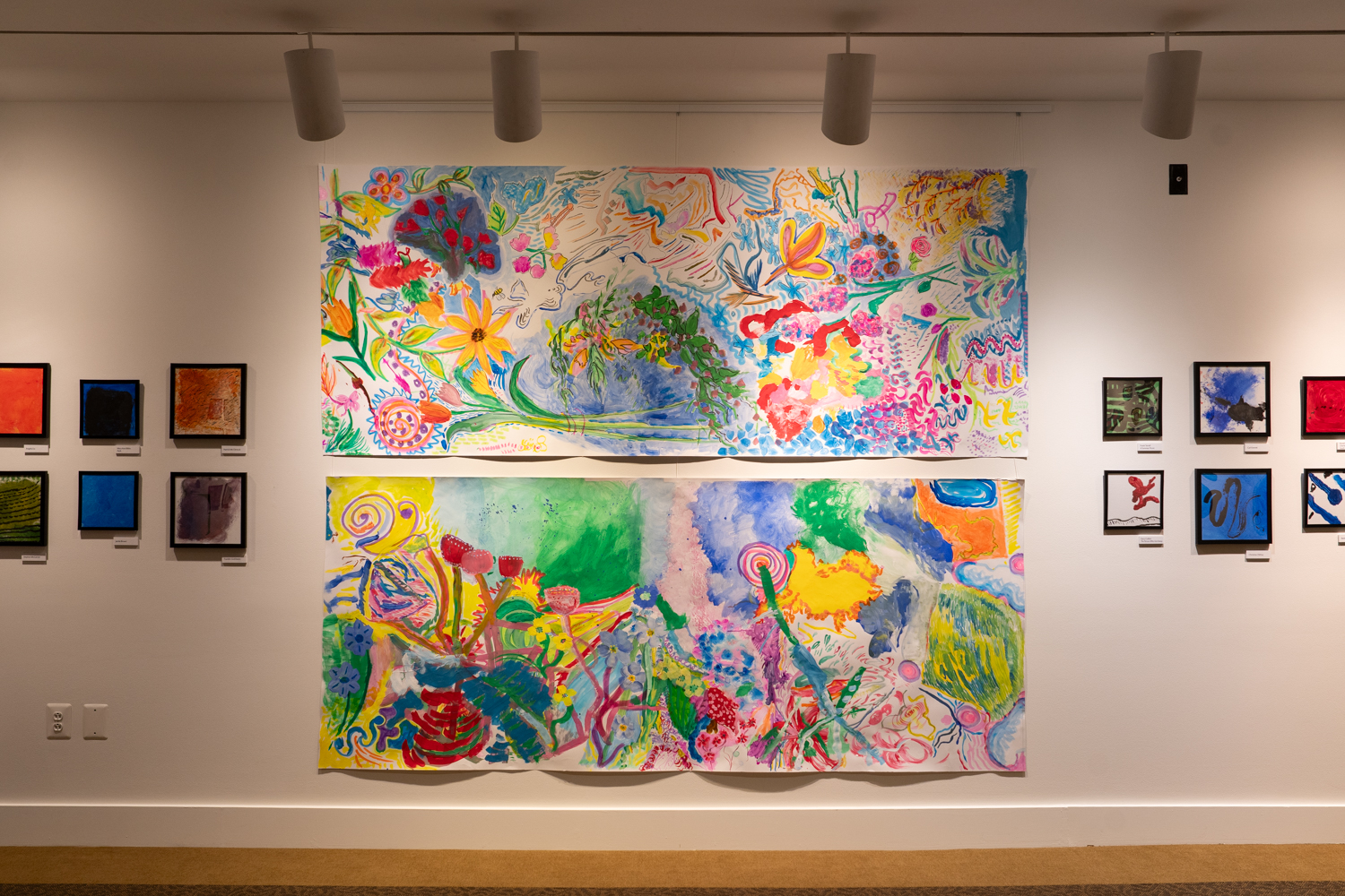 Two large colorful artworks displayed on a wall in between small framed artworks