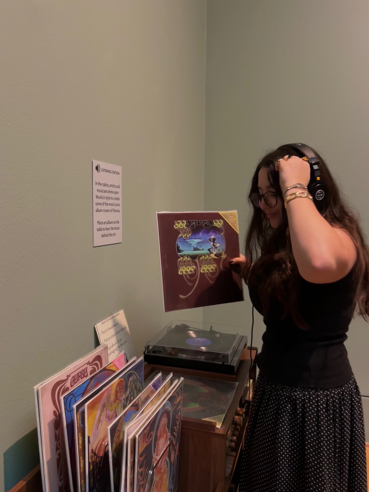 Someone standing by a record player and records listening with headphones on