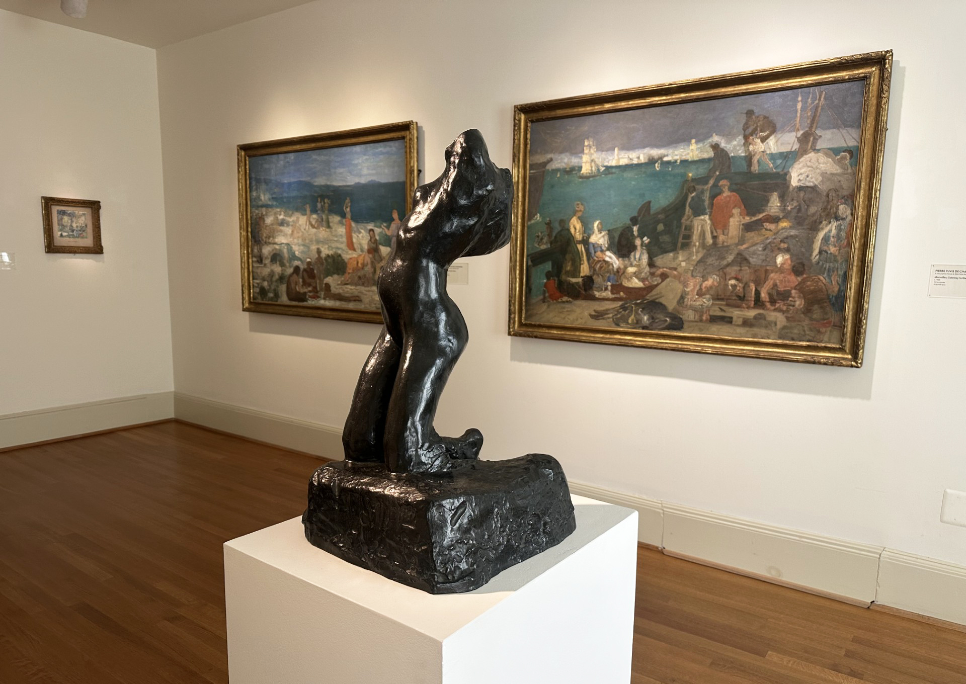 Three paintings on display in a gallery with a sculpture in the center of the room