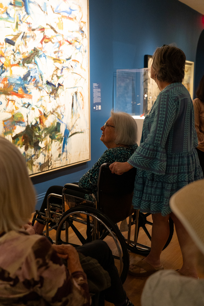 A person standing and a person sitting in a wheelchair looking at a large artwork 