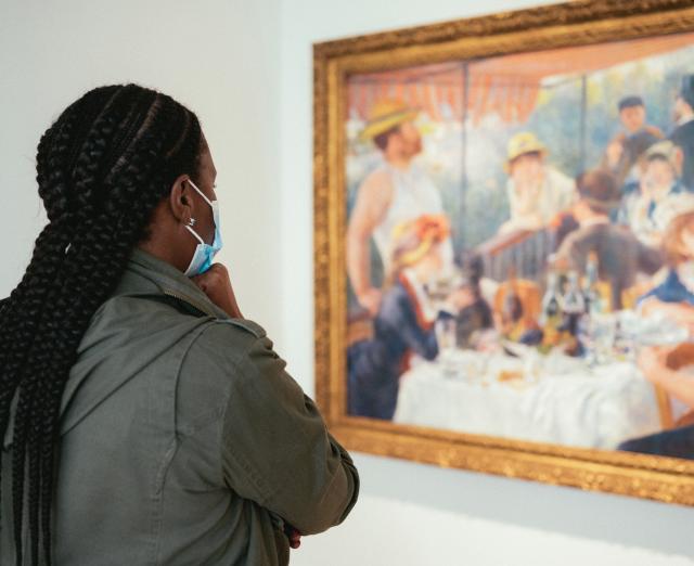 Photograph of woman wearing a mask looking at Renoir's Luncheon of the Boating Party