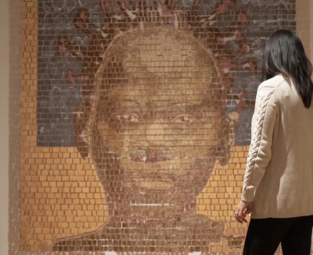 Photograph of a person standing in front of a large artwork of someone's face