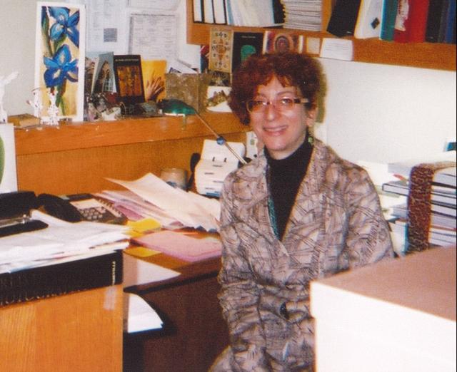 Photograph of a woman at a desk with a lot of papers and boxes