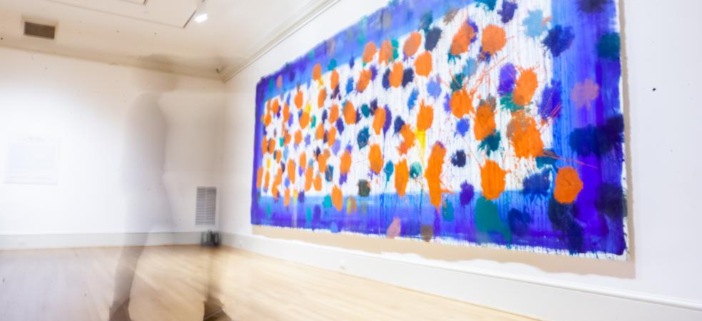 Photo of a blurry figure walking toward a large painting of colorful splatters with a blue border