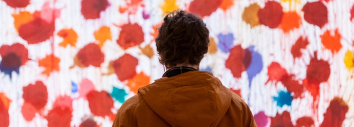 Photograph of a figure looking at a very large artwork with red splotches on a white background