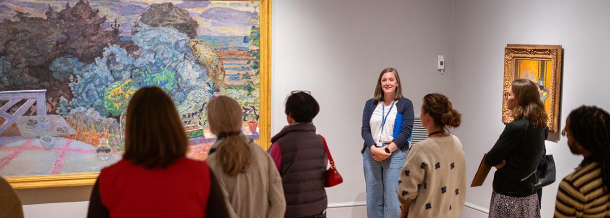 A person giving a talk in a gallery about a large painting on the wall
