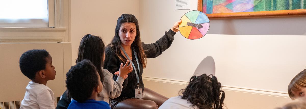 An adult giving a gallery talk to a group of kids sitting on the floor of a gallery