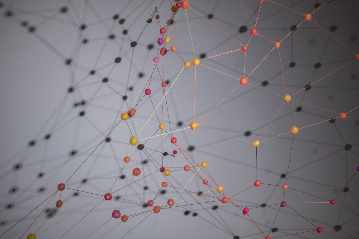 Colorful string and beads connect and cast shadow on the wall behind it