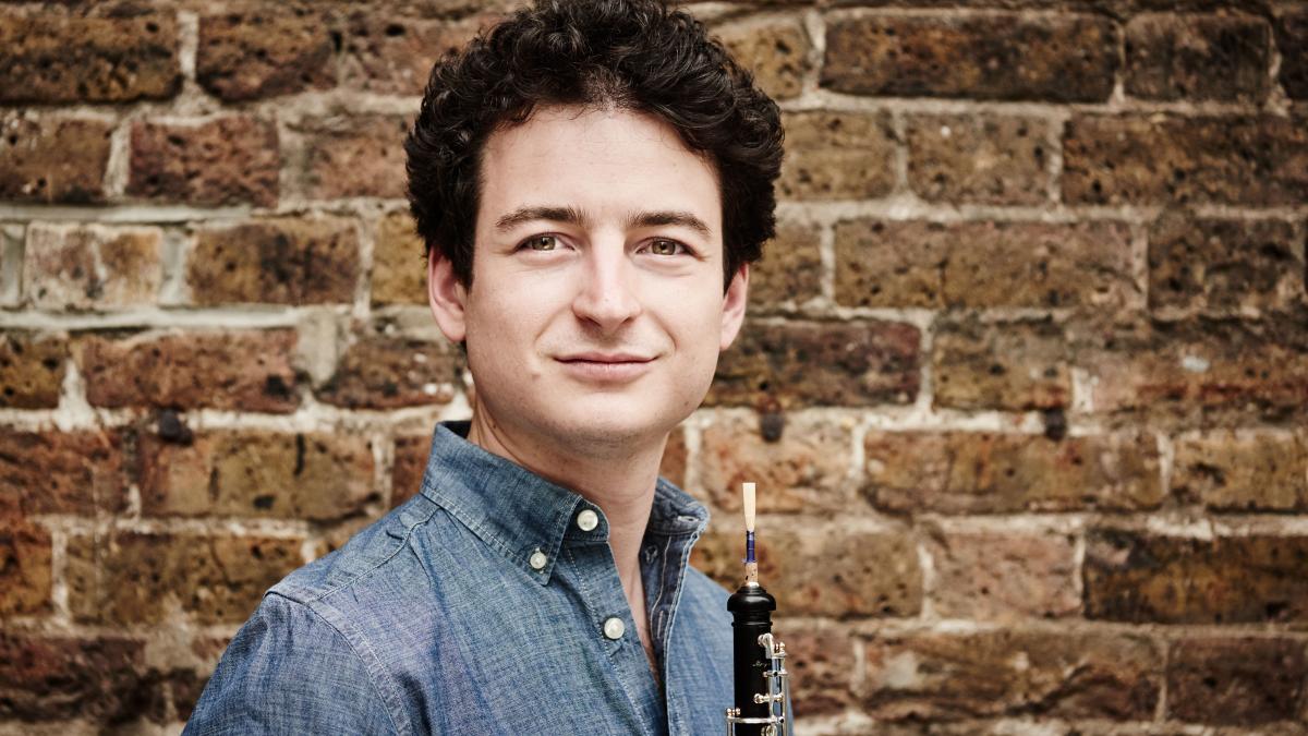 Man with oboe in front of brick wall 