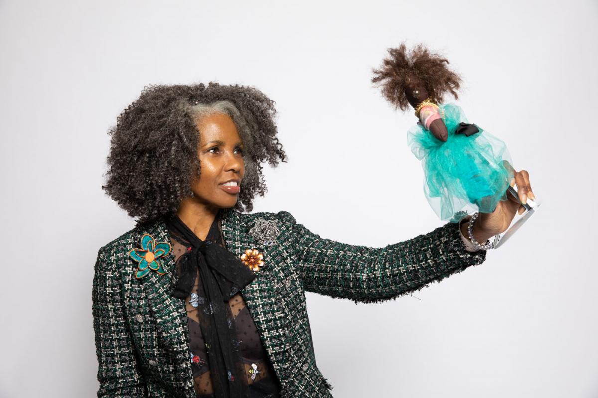 Photo of Sherri Lumpkins holding up and smiling at a Black baby doll