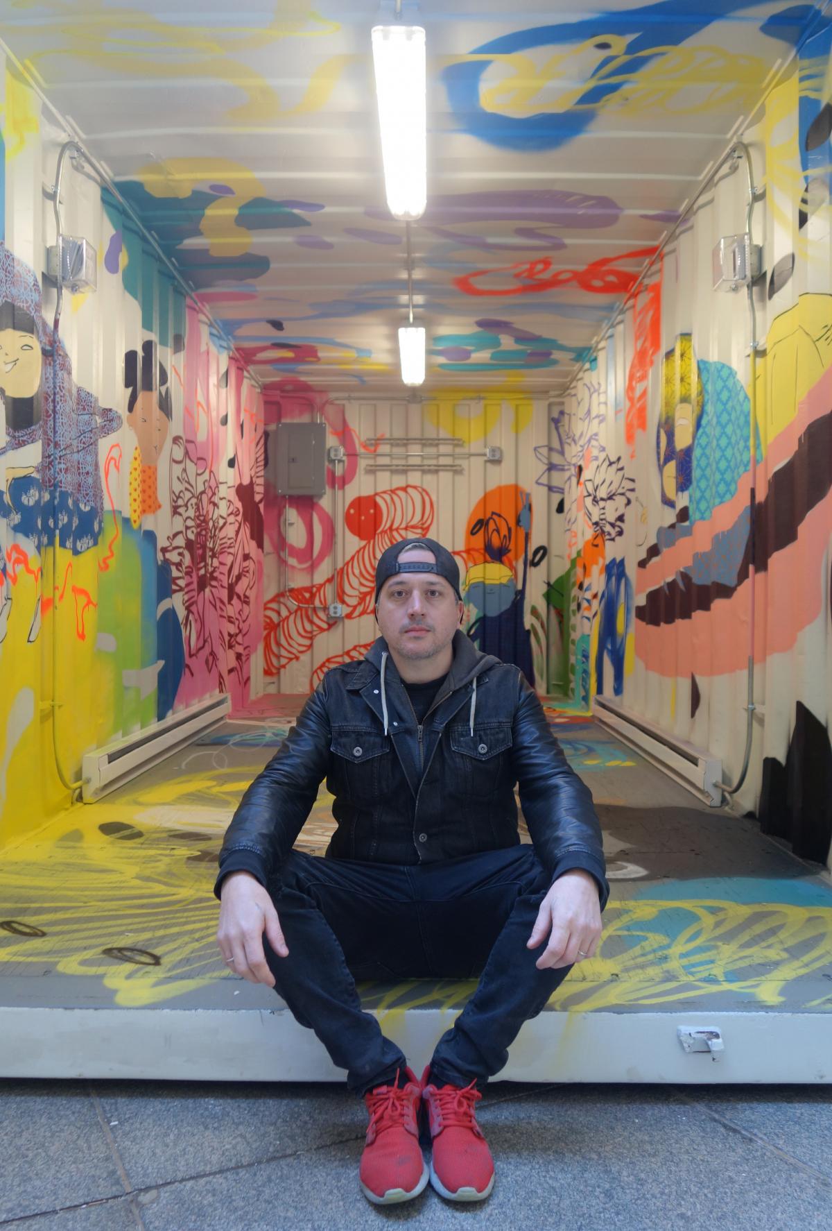 Photo of Kelly Towles sitting on the ground with colorful murals behind him
